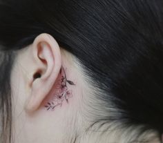 a woman's behind the ear has a small flower tattoo on it