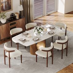 a dining room table with white chairs and plates on the top, in front of a large window