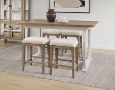 a dining room table with four stools and a vase on the wall behind it