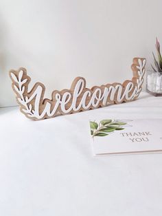 a wooden welcome sign sitting on top of a table next to a card and potted plant