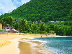 a sandy beach next to a lush green mountain