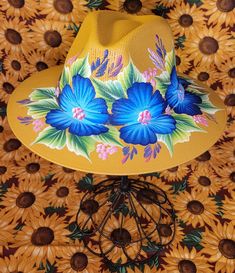 Hand painted mustard yellow sun hat with a touch of bright blue floral design Blue Summer Straw Hat For Festivals, Spring Floral Print Brimmed Sun Hat, Summer Wide Brim Hat With Floral Print, Wide Brim Hat With Floral Print For Summer, Wide Brim Floral Print Hat For Summer, Spring Beach Hats With Floral Print, Spring Sun Hat With Curved Brim And Floral Print, Summer Floral Print Brimmed Hat, Handmade Flower Hats For Summer