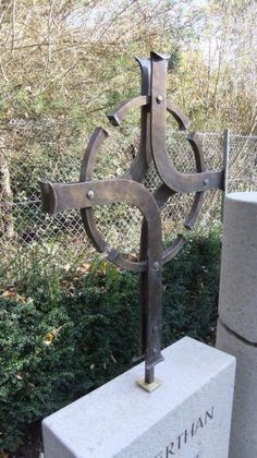 an iron sculpture in the middle of a grassy area with bushes and trees behind it