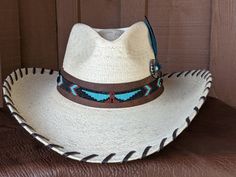 The Maverick starts with a Mexican soft palm leaf hat body that has a 3 3/4" brim and 5 1/4" crown. Hand laced in chocolate brown leather lace. The beaded hatband has a Thunderbird pattern and then mounted on distressed leather. The back of the band has a deer antler bead for accent. Starburst turquoise Concho and deep blue/green decorative feather completes the hat. All hats are made to order. Allow up to 4 weeks for your hat to ship. Brown High Crown Country Hat, High Crown Brown Country Hat, Brown High Crown Fedora For Country Events, Western Style Brown Panama Hat With Flat Crown, Western Brown Panama Hat With Flat Crown, Custom Brown Hat Bands For Ranch, Brown High Crown Fedora For Western-themed Events, Rustic High Crown Hat For Rodeo, Western High Crown Fedora In Brown