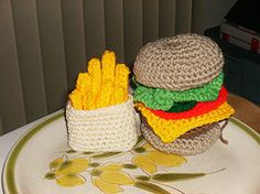 a crocheted hamburger and french fries are on a white plate with green trim