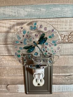 a light switch cover with a glass dragonfly on it's side and attached to a wooden wall