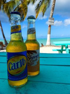 two bottles of beer sitting on top of a blue picnic table next to the ocean