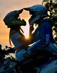 two people sitting on a motorcycle with the sun setting in the back ground behind them