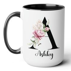 a white and black coffee mug with pink flowers on the front, and an initial