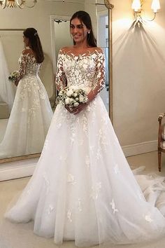 a woman standing in front of a mirror wearing a white wedding dress with long sleeves