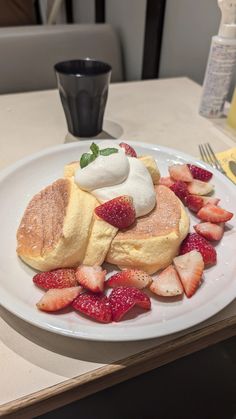 a white plate topped with pancakes covered in whipped cream and strawberries