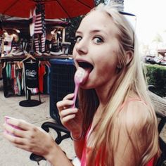 a woman with long blonde hair is eating something while sitting on a bench in front of an umbrella