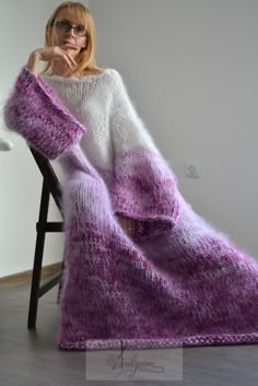 a woman is sitting in a chair wearing a purple and white knitted blanket,