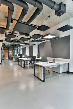 an empty office with white desks and black pipes hanging from the ceiling above them