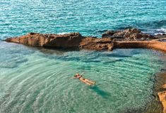 two people are swimming in the water near some rocks and blue water with green algae