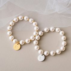 two bracelets with white pearls and gold accents on a beige surface, one is personalized