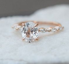 an oval cut engagement ring with two side stones on top of it, sitting on a rock