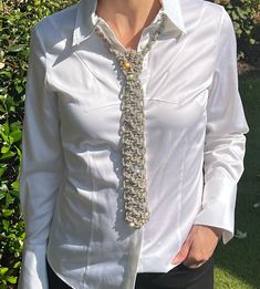 a woman wearing a white shirt and a silver neck tie in front of some bushes