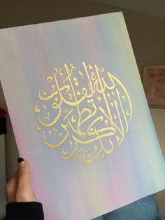 a person holding up a painting with arabic writing on it