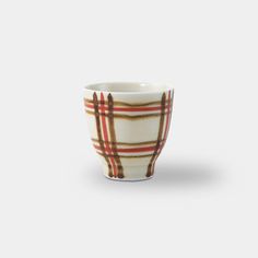 a white cup with brown and red plaid designs on the outside, sitting in front of a gray background