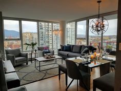 a living room filled with furniture next to large windows and a chandelier hanging from the ceiling