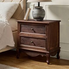 a nightstand with a lamp on top of it next to a bed