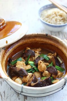 a bowl filled with meat and vegetables on top of a wooden table next to rice