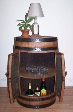 a wooden barrel with wine glasses and bottles in it on top of a table next to a lamp