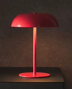 a red table lamp sitting on top of a black counter next to a brown wall