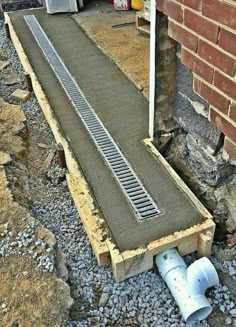 a drain in the ground next to a brick wall and some pipes on the ground