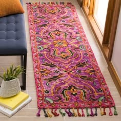 a colorful rug with tassels on the floor next to a blue chair and potted plant