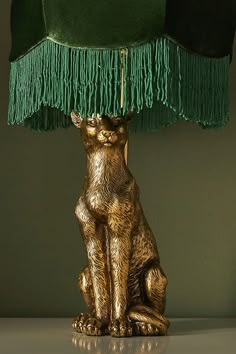 a gold cat sitting under a green lamp on top of a white table with a black shade