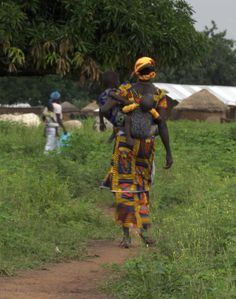 a woman walking down a dirt road carrying a baby