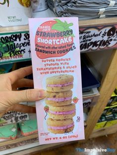 a person holding up a box of strawberry shortcake sandwiches with pink frosting on them