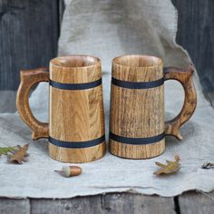 two wooden mugs sitting next to each other on top of a cloth covered table