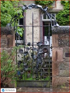 an iron gate with flowers on it in front of a brick wall and window frame