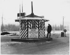 a black and white photo of a man standing in front of a building with a sign on it