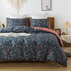 a bed covered in blue and pink floral comforter sets on a wooden floor next to a lamp