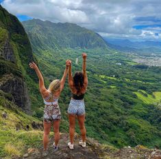 two young women standing on top of a mountain with their arms raised in the air