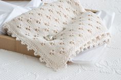 a white crocheted blanket sitting on top of a cardboard box next to pillows