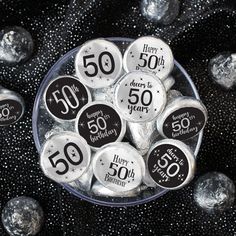 a glass bowl filled with lots of happy 50th birthday button pins on top of black and silver foil