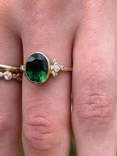 A perfect emerald green Tourmaline is set in Emily's 14k gold Trefoil cluster setting with a freeform band. We originally saw this as being a unique engagement ring but it would be just as wonderful as an everyday bit of sparkle and looks phenomenal with our halo bands Approximate stone size: 10mm x 8mm TCW tourmaline: 2.5ct TCW diamonds: .12ct Mohs Stone Hardness: 7.5-8 This one of a kind piece is handmade in Emily's Hudson Valley studio. If you have questions about sizing, shipping or need hel Oval Green Rose Cut Diamond Rings, Green Cluster Ring With Rose Cut Diamonds, Heirloom Green Emerald Ring With Bezel Setting, Unique Emerald Ring For May Birthstone, Green Emerald Cluster Ring With Rose Cut Diamonds, Green 14k Gold Cluster Ring, Green Tourmaline Jewelry With Halo Setting, Unique Emerald Ring With Prong Setting, Green Oval Cluster Ring Fine Jewelry