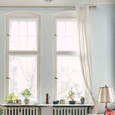 a living room with two large windows and a radiator in the corner,