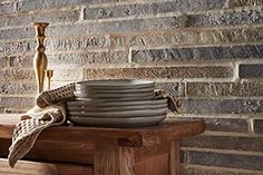 a stack of plates sitting on top of a wooden table next to a brick wall