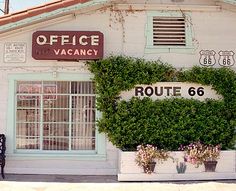 an old building with plants growing on the side and signs above it that read route 66