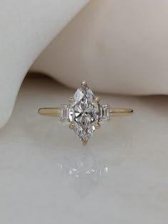 an engagement ring with three stones on it, sitting on a white surface next to a pillow