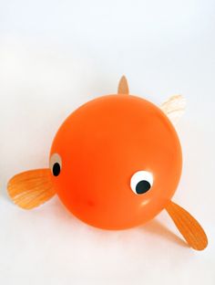 an orange plastic fish with eyes on it's head and tail, sitting in front of a white background