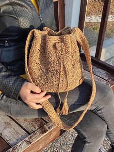 a woman is sitting on a bench holding a brown handbag with tassels