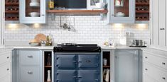 a blue stove top oven sitting inside of a kitchen next to white cupboards and drawers