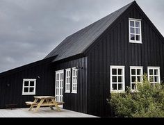 a black house with white windows and a picnic table in front of it on a cloudy day